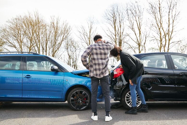 Young male and female drivers looking at damaged car