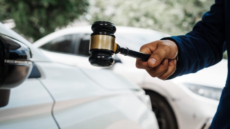 lawyer holding a wooden gavel and standing in front of a car