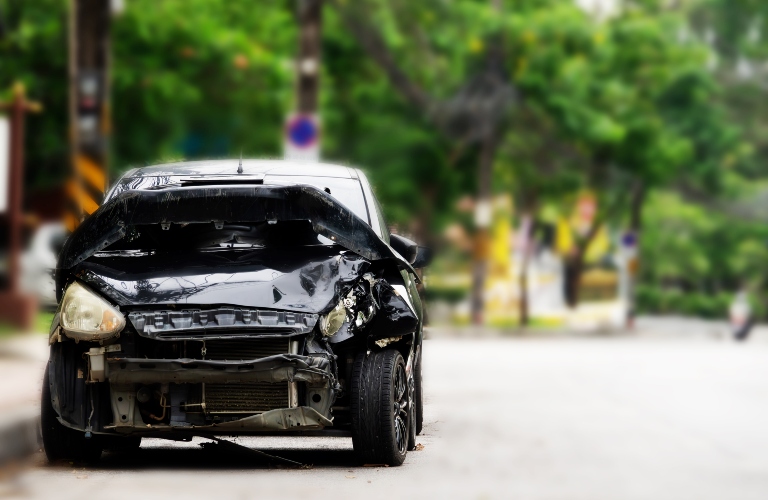 A black car with a smashed front end is parked on the side of the road